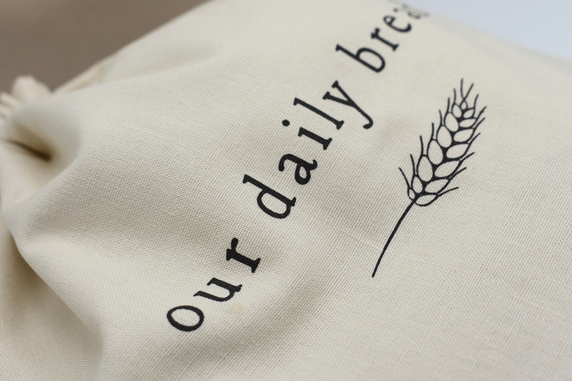 Beige drawstring bag with 'our daily bread' text and wheat stalk printed with non-toxic ink 